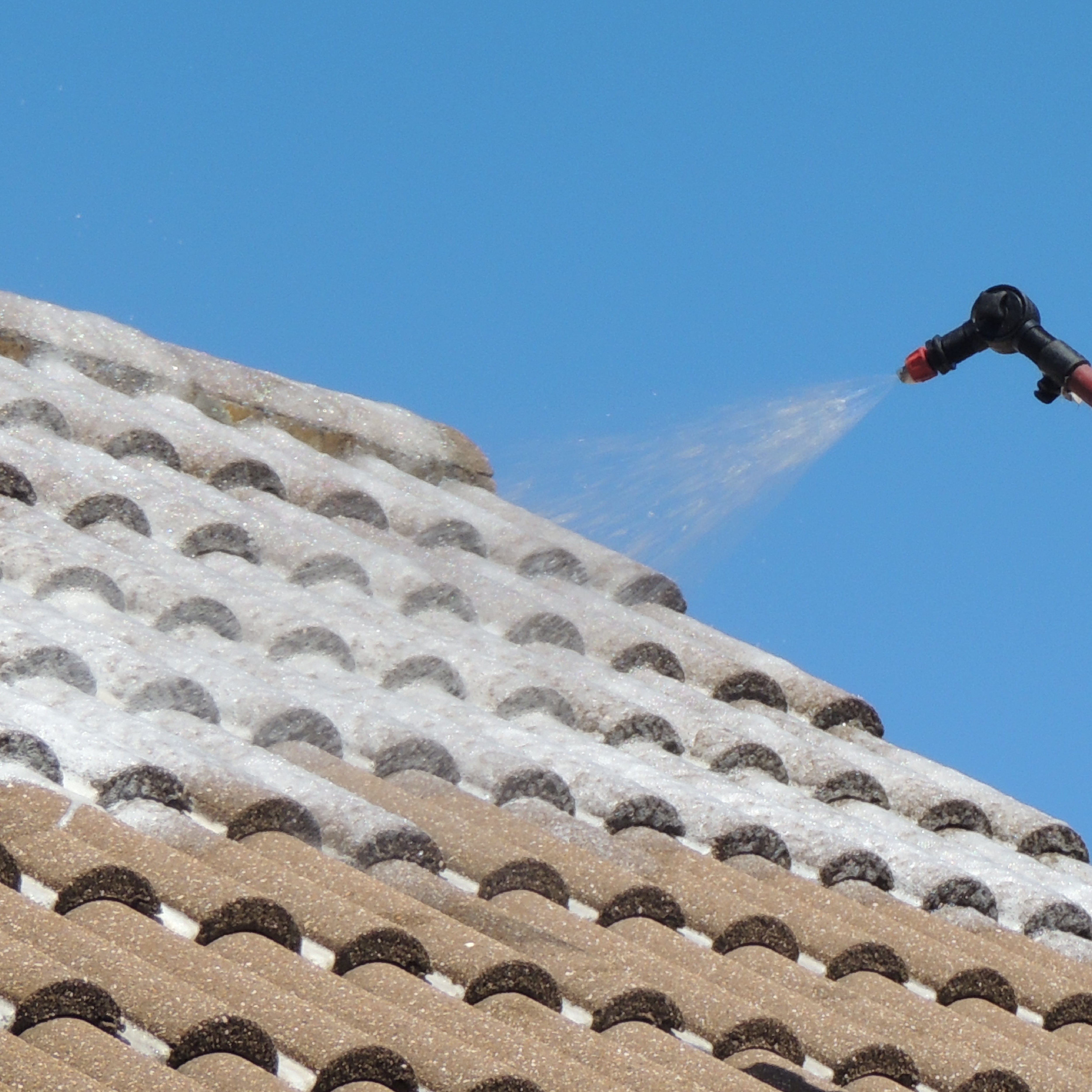 An image of a telescopic sprayer cleaning roof tiles with hard surface cleaner fluid.